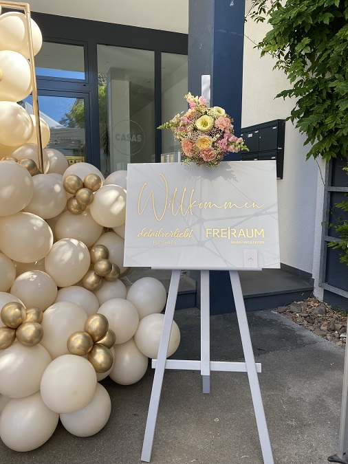 Weiße und goldene gebundene Luftballons hinter weißem Hochglanz Willkommensschild