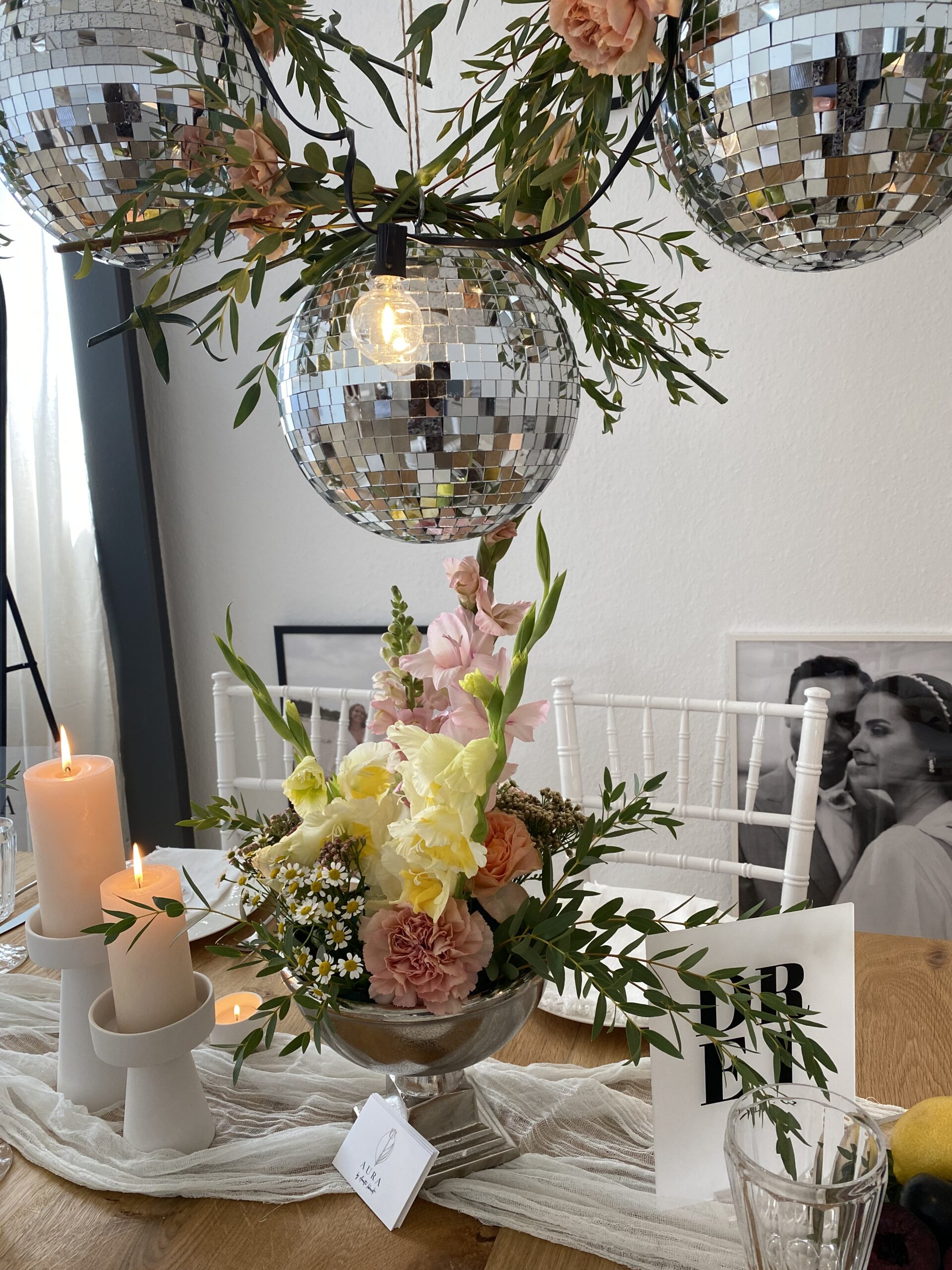 Discokugeln mit Lampen über einem blumendekorierten Tisch mit Kerzen für Brautpaare