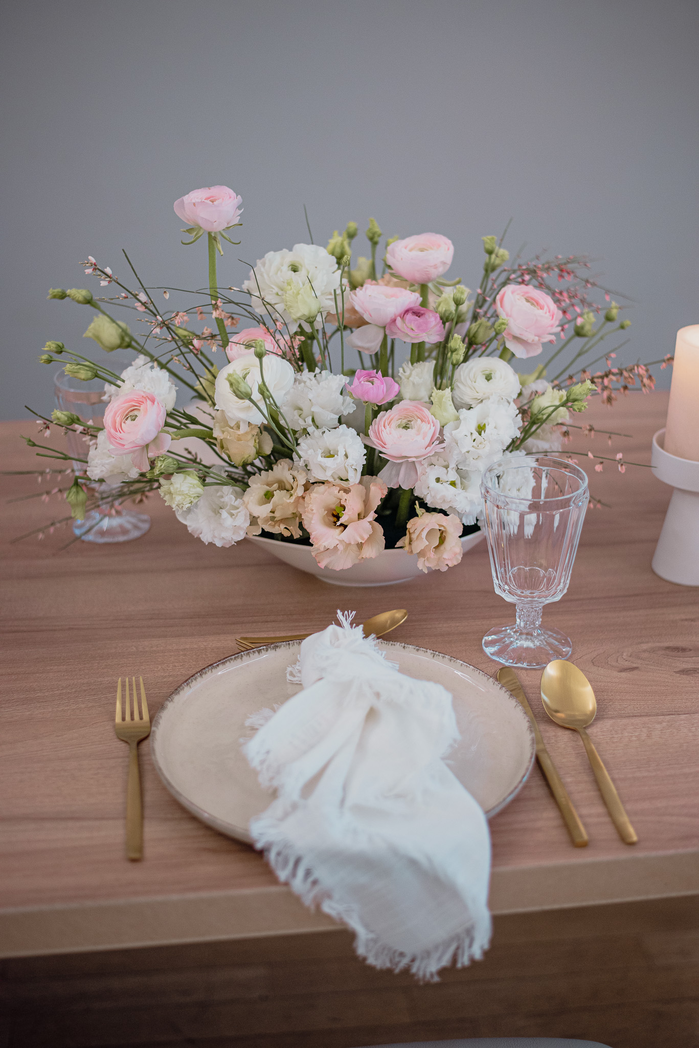 Gedeckter Tisch mit goldenem Besteck und einem weiß, rosa Blumengesteck