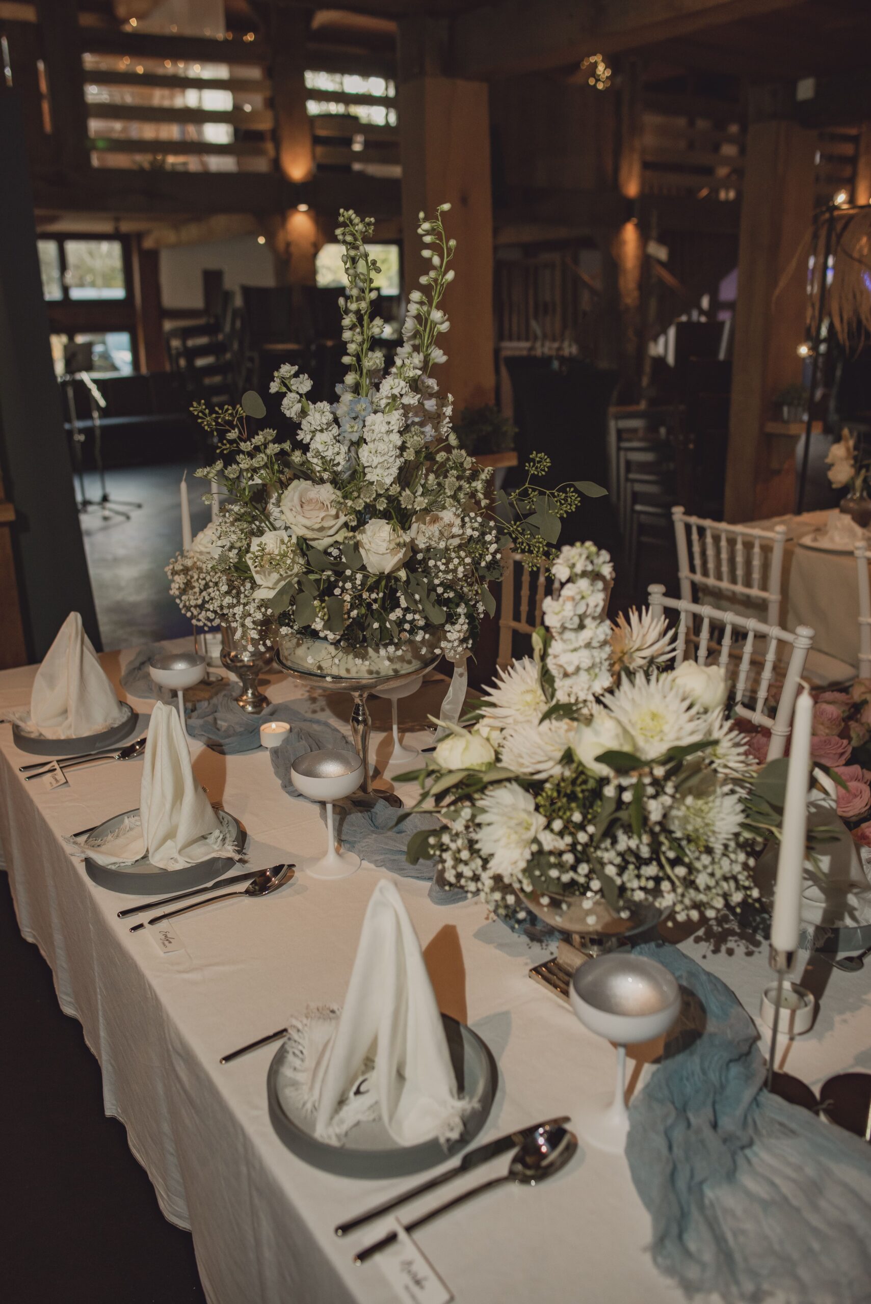 Pompöse Blumensträuße in Weiß mit Silberakzenten auf gedecktem Tisch