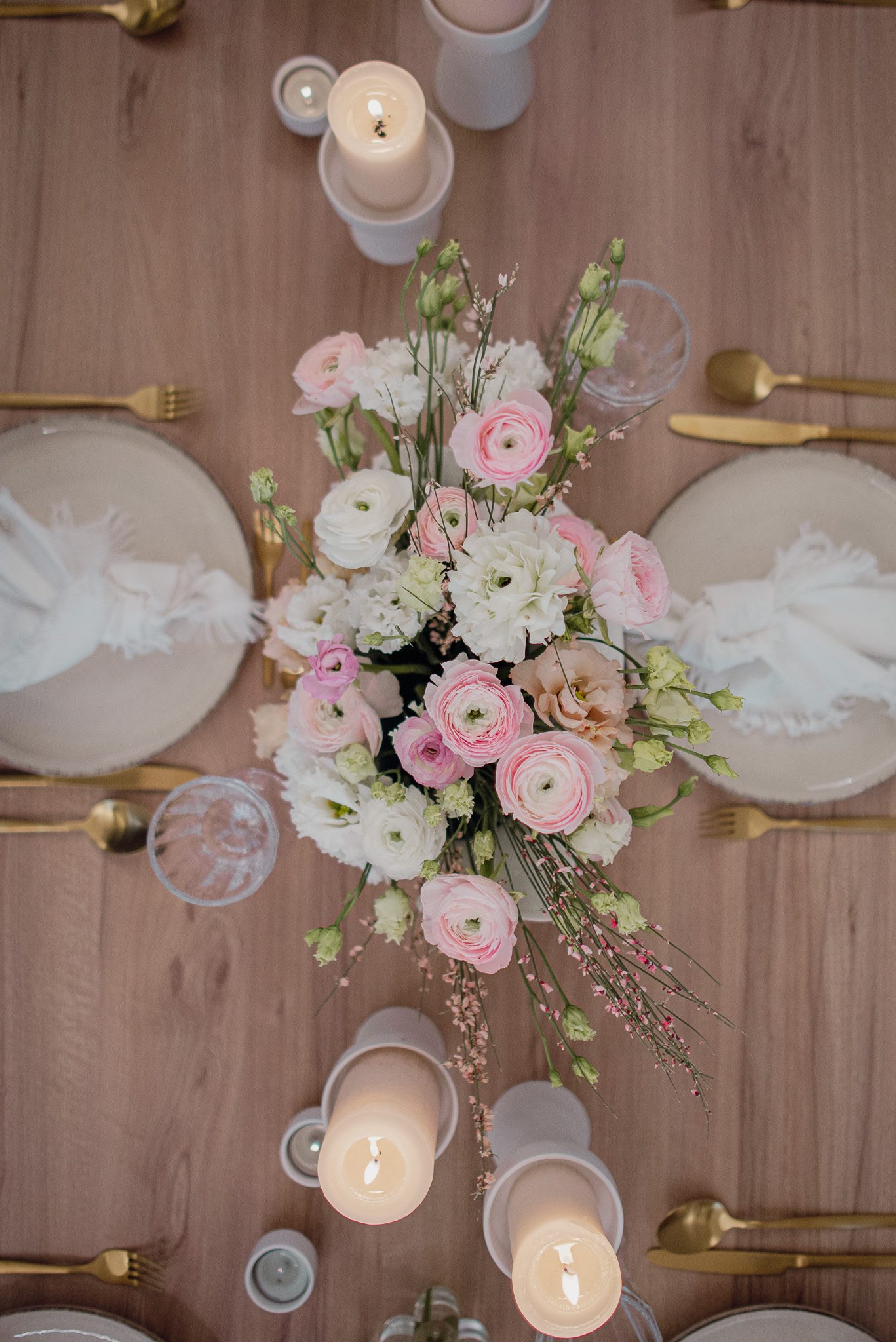 Gedeckter Tisch mit goldenem Besteck, weißen Kerzen und einem weiß, rosa Blumenstrauß