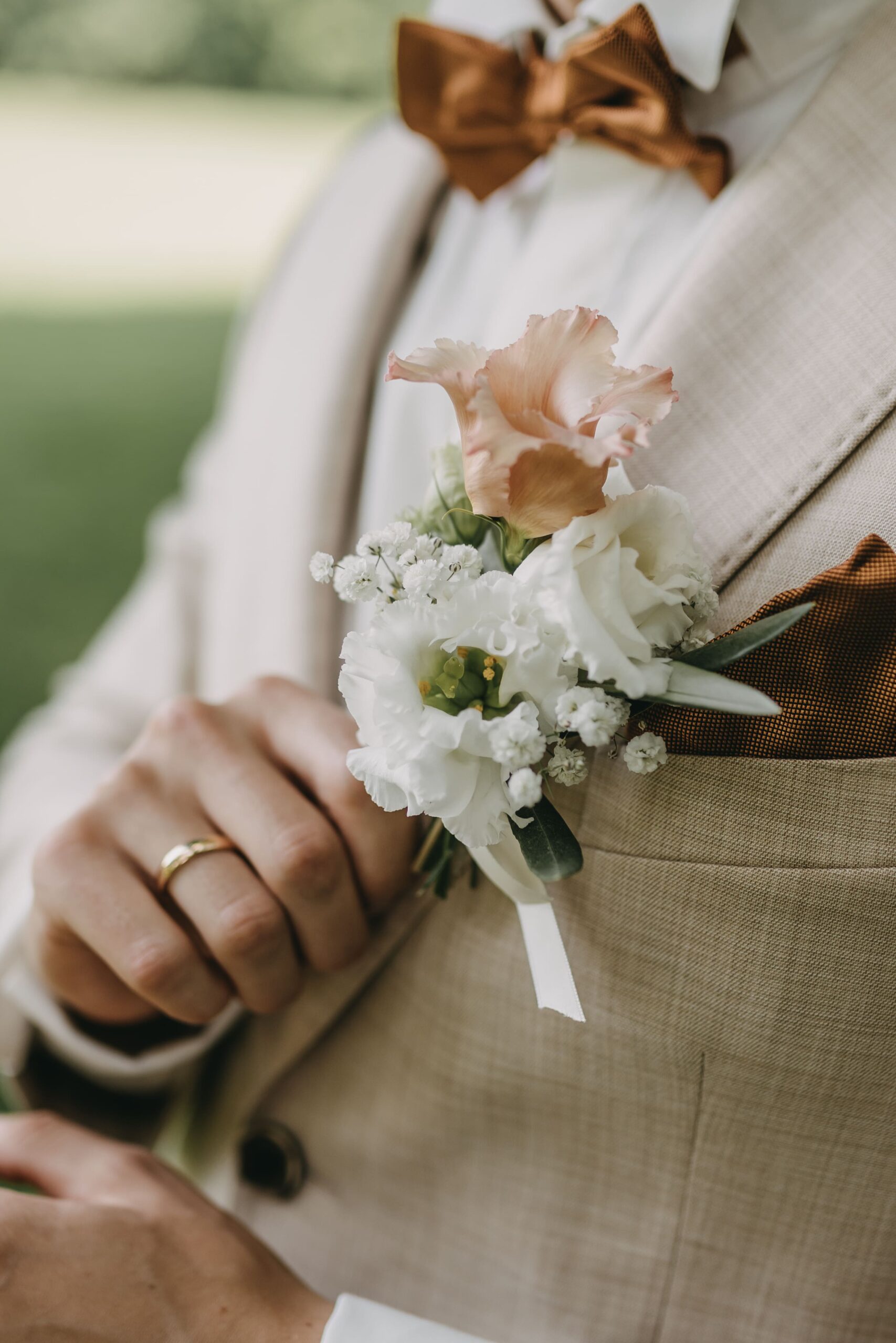 Mann im Sakko hält mit seiner rechten Hand an seinem Ansteckstrauß fest mit einem Ring am Ringfinger