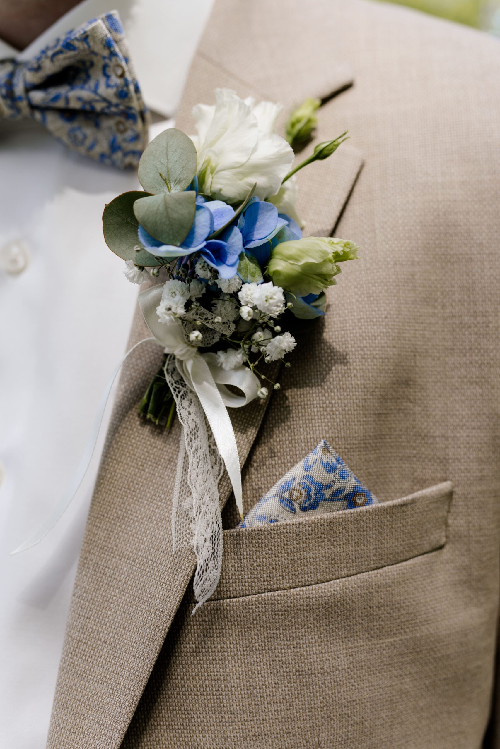 Ein Mann in einem beigen Sakko mit einem Ansteckstrauß mit weißen und blauen Blumen