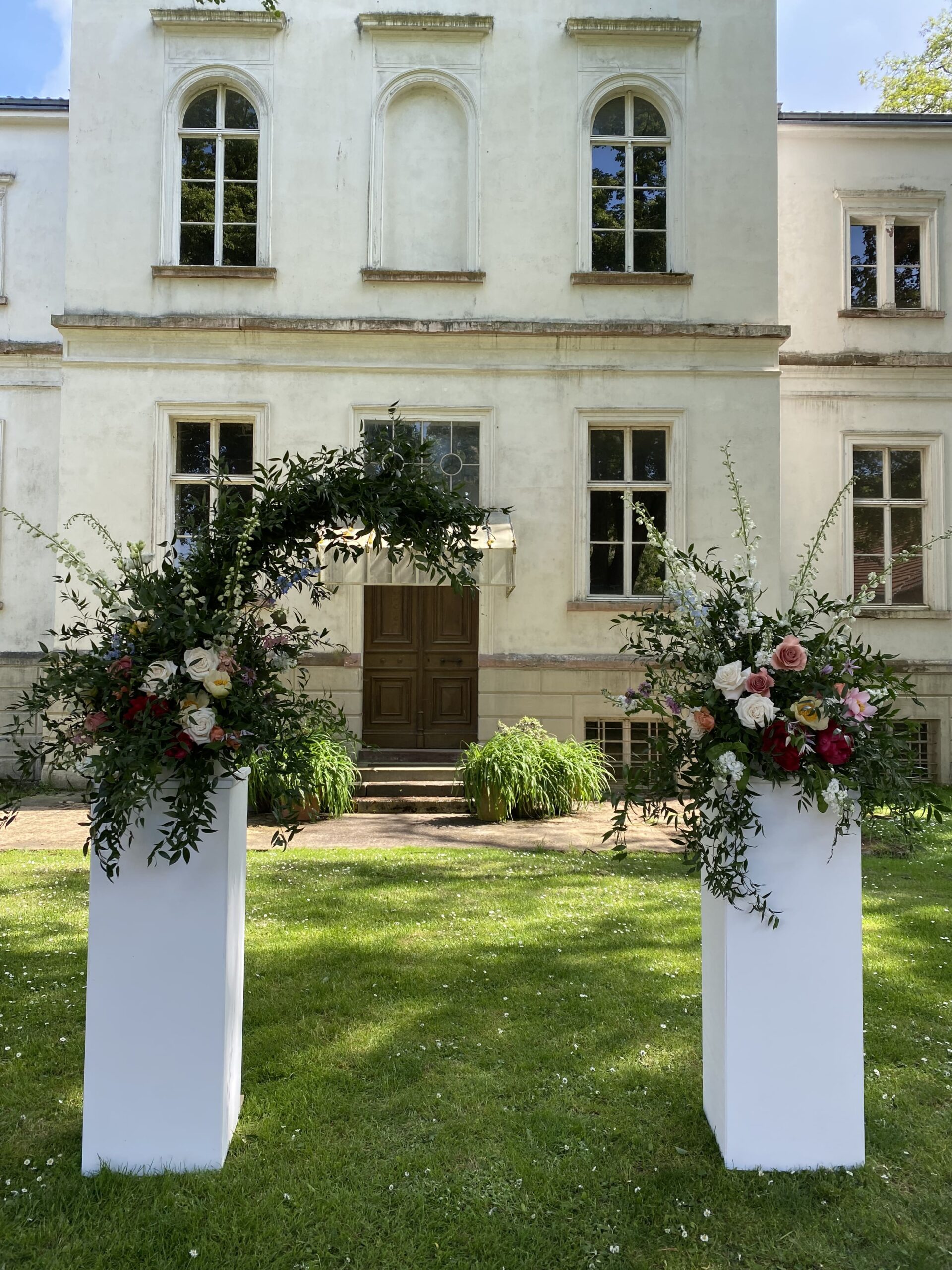 Zwei große, weiße Blöcke vor einem Eingang mit großen Blumengestecken oben drauf