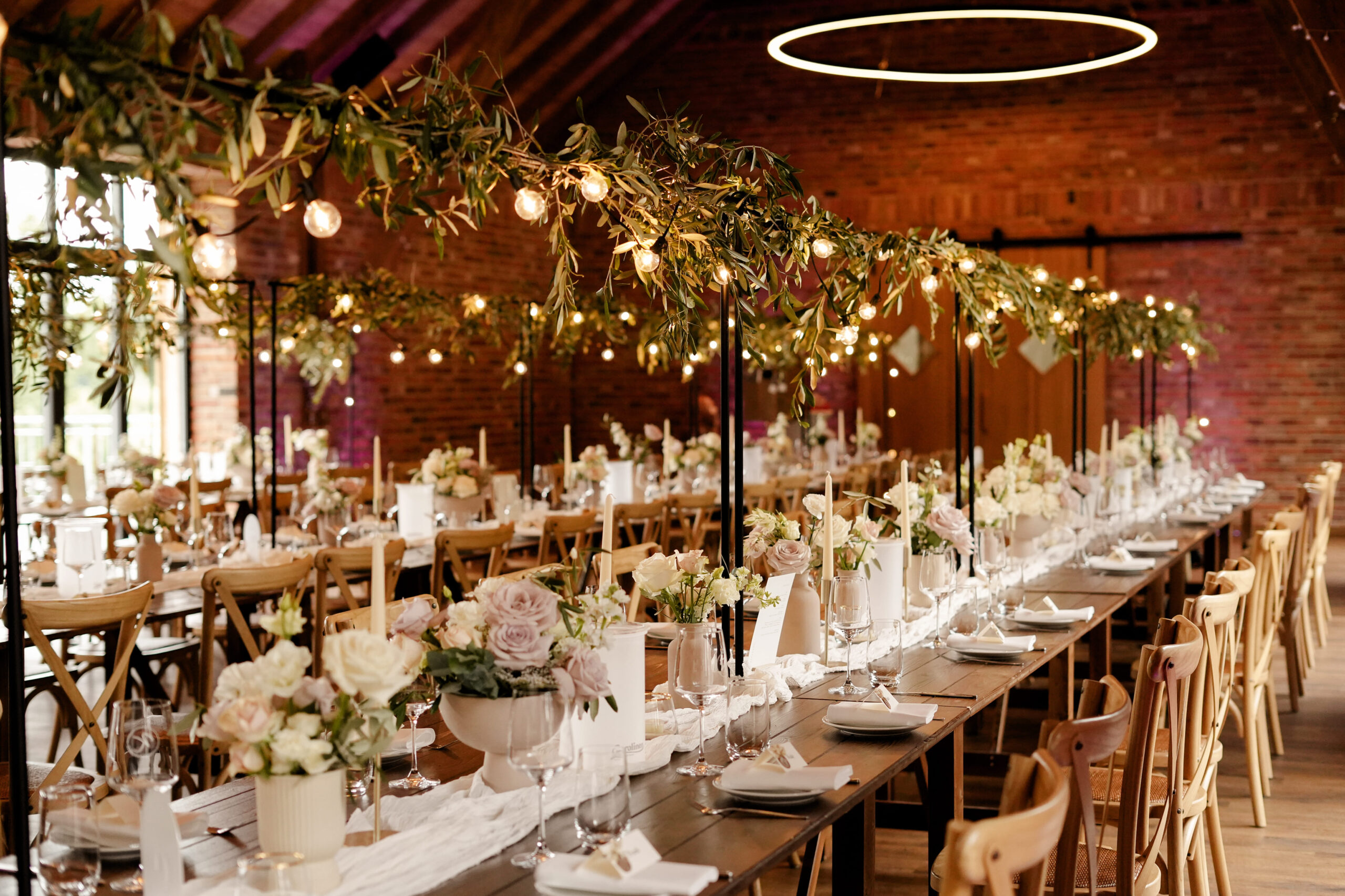 Ein gedeckter Tisch für Hochzeitsgäste mit einer Girlande unter Grünschnitt auf einer Teleskopstange über dem Tisch