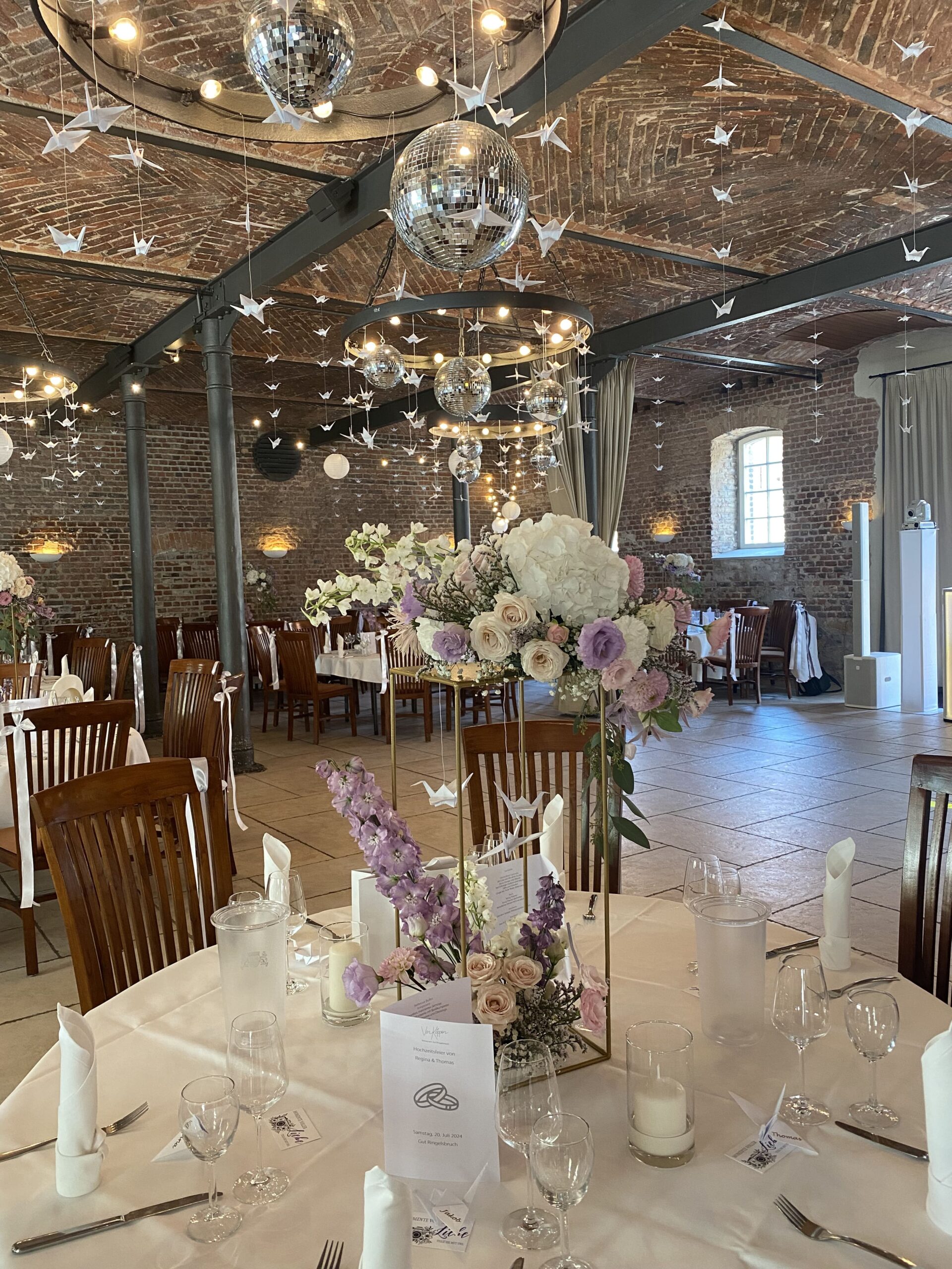 Discokugeln an der Decke neben vielen kleinen Schwalben aus Papier über einem gedeckten Tisch mit Kerzen und Blumen auf einem Glasblock