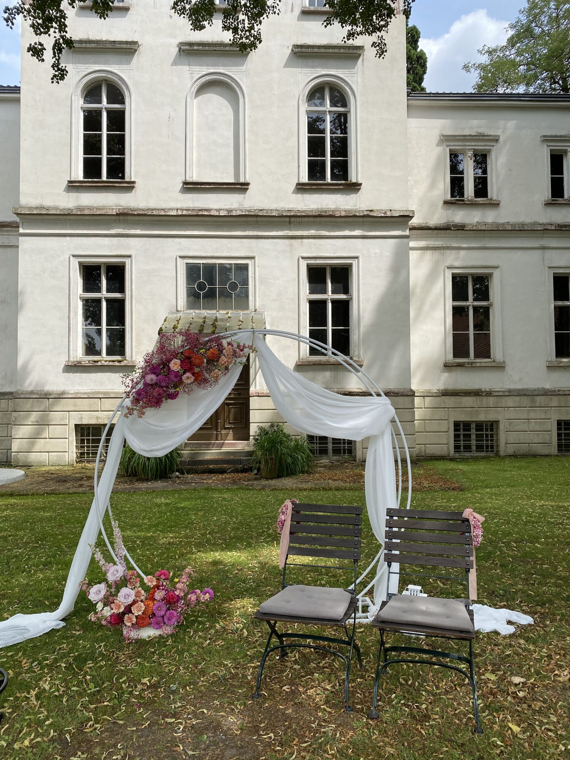 Blumenbogen vor einem Eingang mit weißem Schleier und pinken und roten Blumen