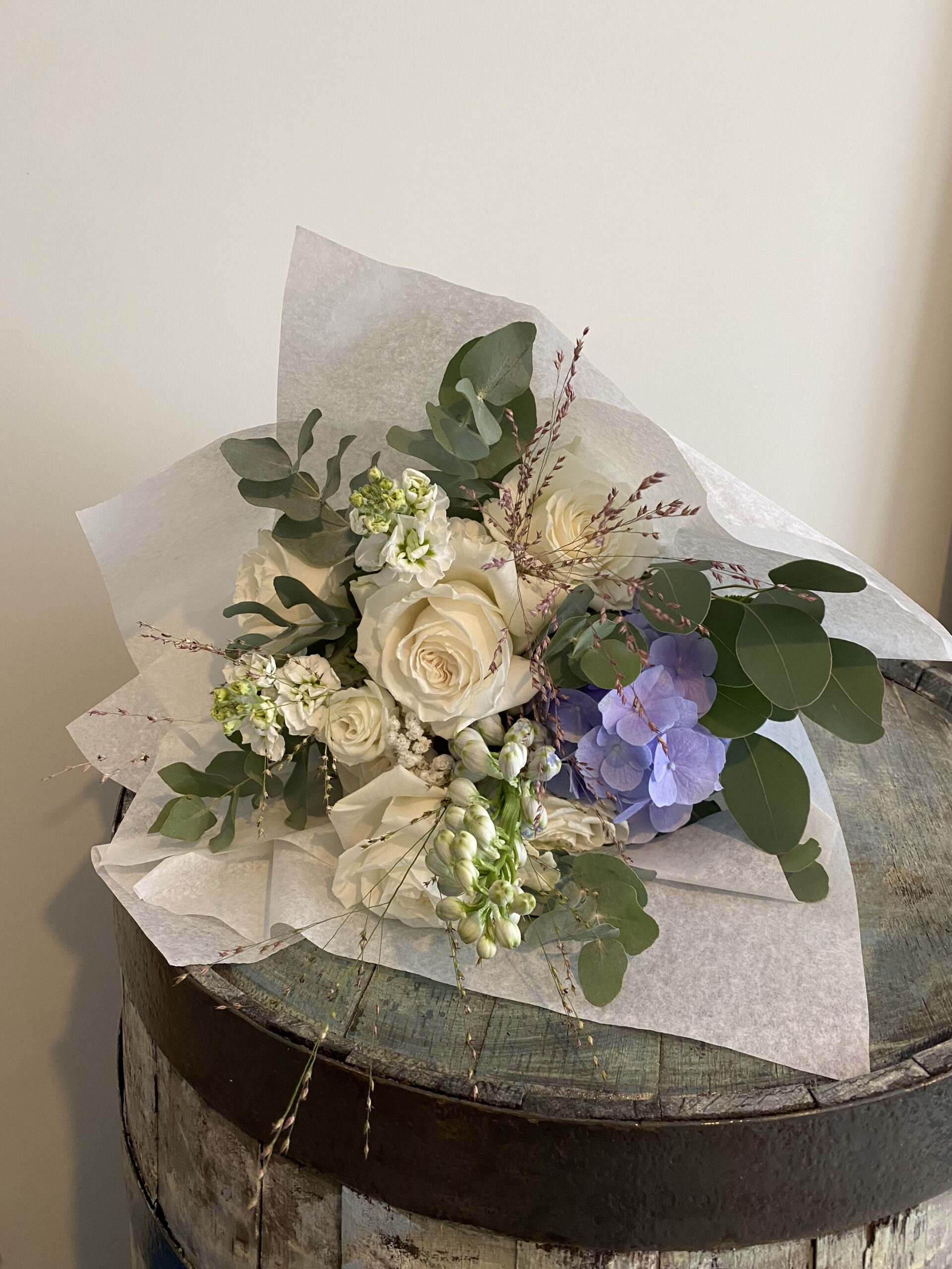 Kleiner, heller Blumenstrauß auf einem hellen Holzfass