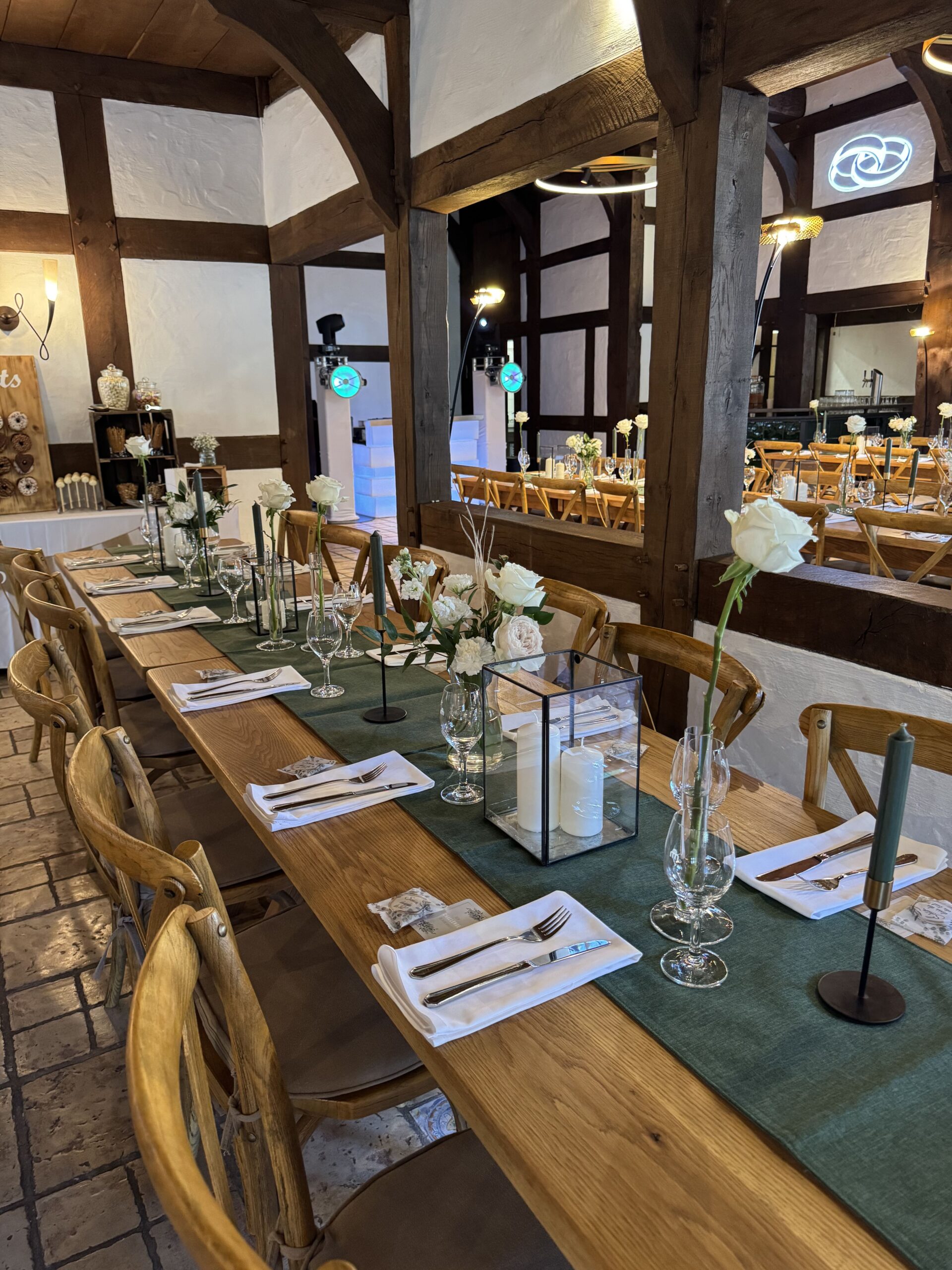 Tische und Stühle aus Echtholz mit Silberbesteck, weißen Blumen und dunklen Stehkerzen