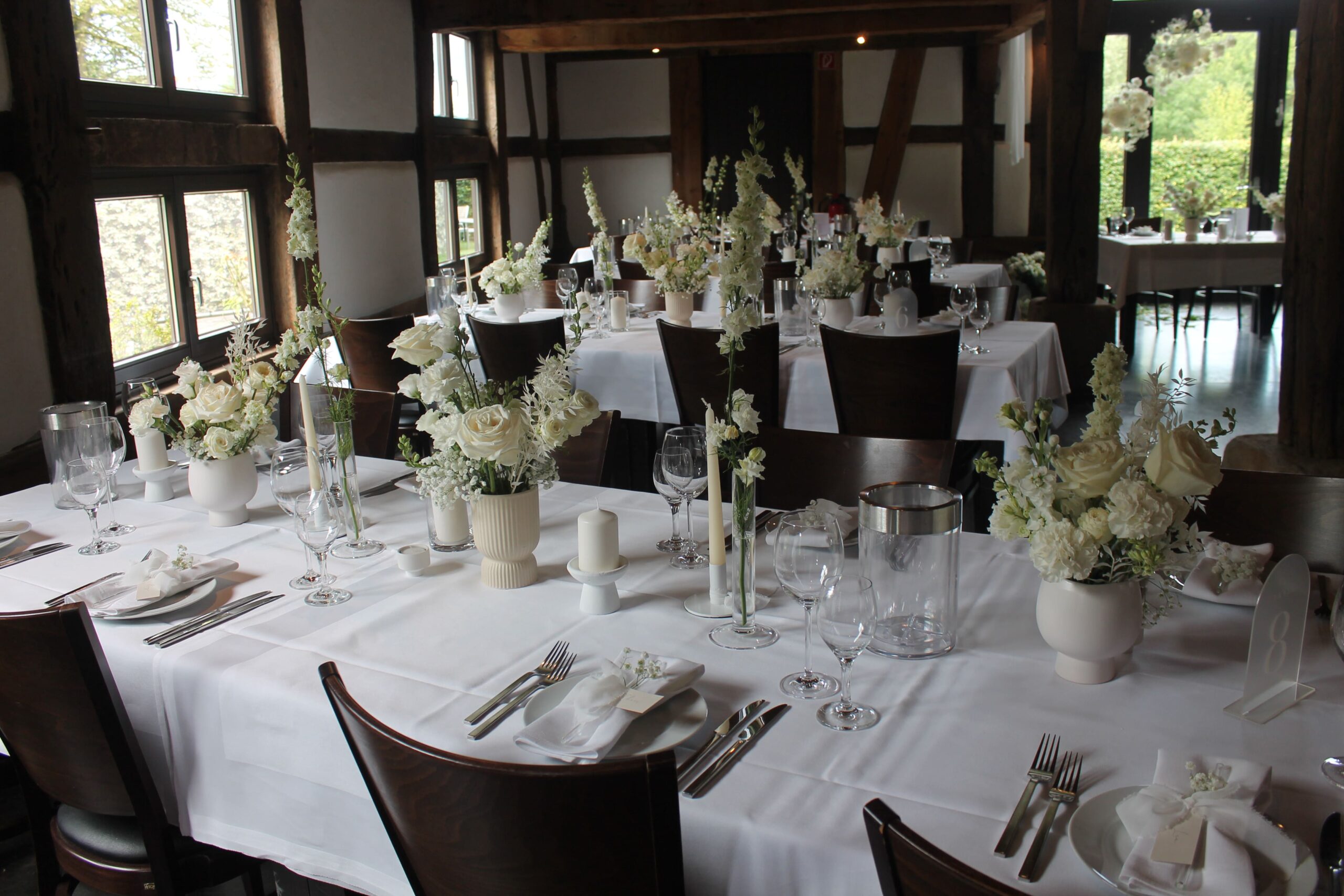 Weiß gedeckte Tische in einem rustikalen Lokal mit großen weißen Rosen